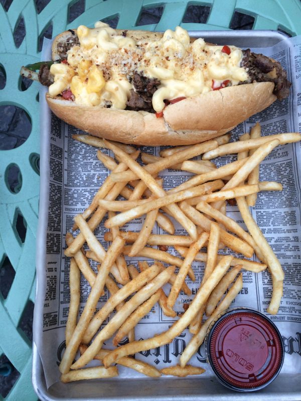 A hot dog with cheese and toppings next to french fries.