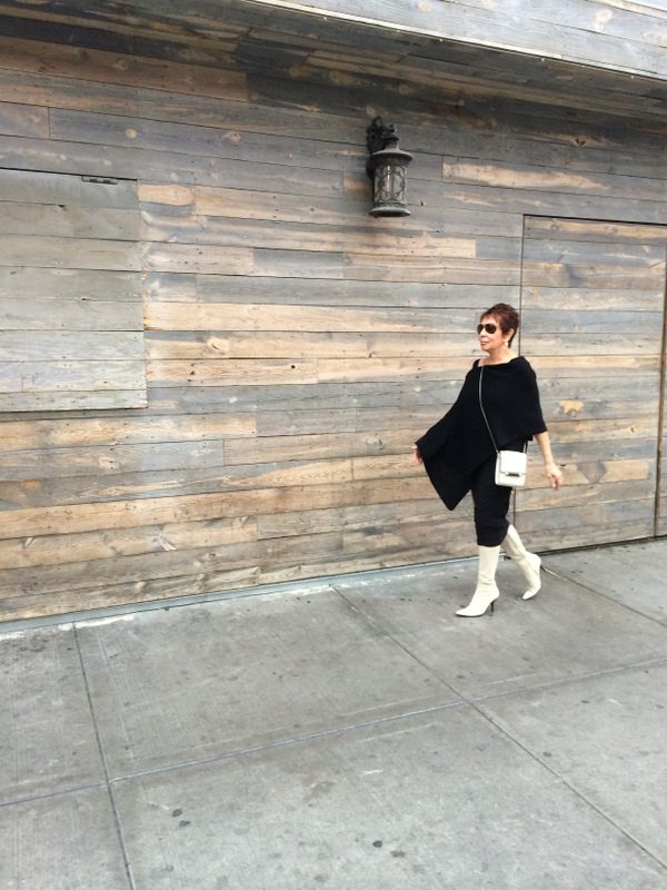 A woman in white boots and black outfit walking on the sidewalk.
