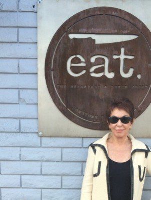 A woman standing in front of an eat sign.