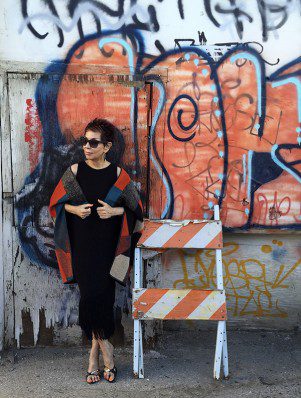 A woman in black dress standing next to graffiti.