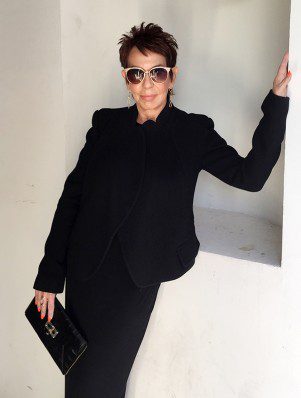 A woman in black suit and sunglasses posing for the camera.
