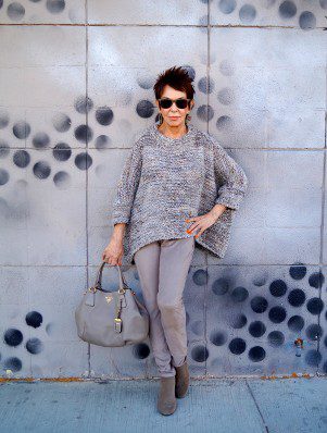 A woman standing in front of a wall with her purse.