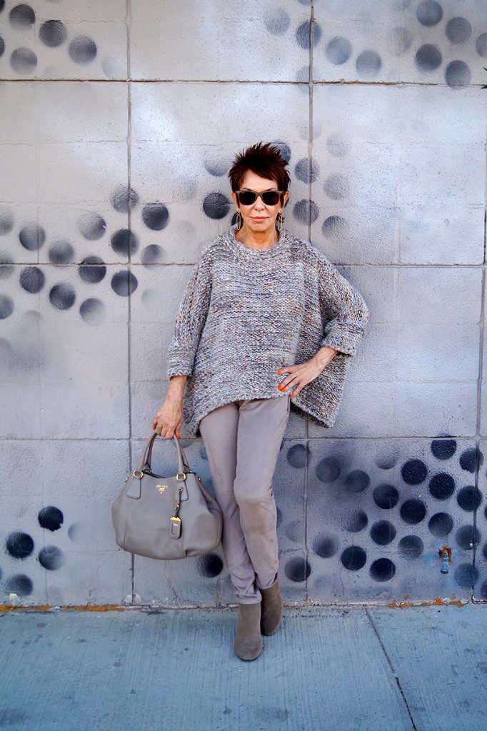 A woman standing in front of a wall with her purse.