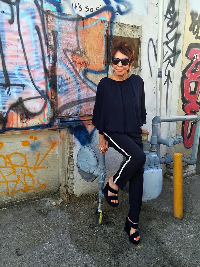 A woman in black shirt and white pants sitting on a skateboard.