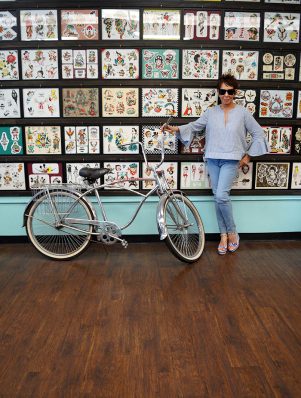 A woman standing next to a bicycle in front of a wall.