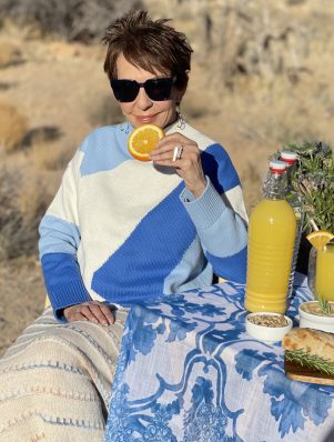 Dorrie wearing a Blue and White Sweater by a Picnic Table Holding an Orange Slice